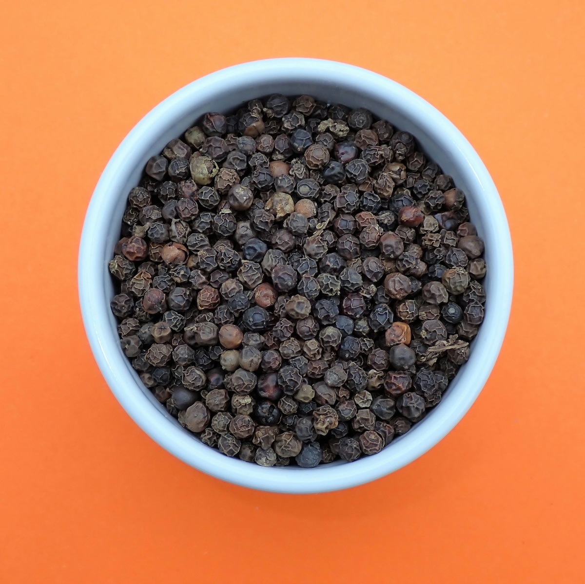 A bowl of black peppercorns on an orange coloured surface