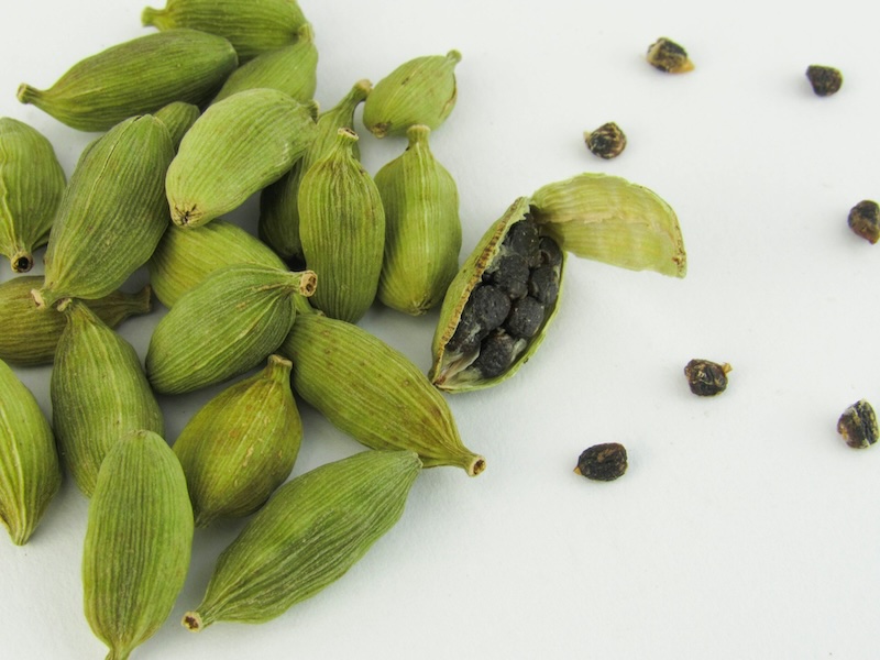 Cardamom pods on a table. One pod is cracked open with seeds laying nearby