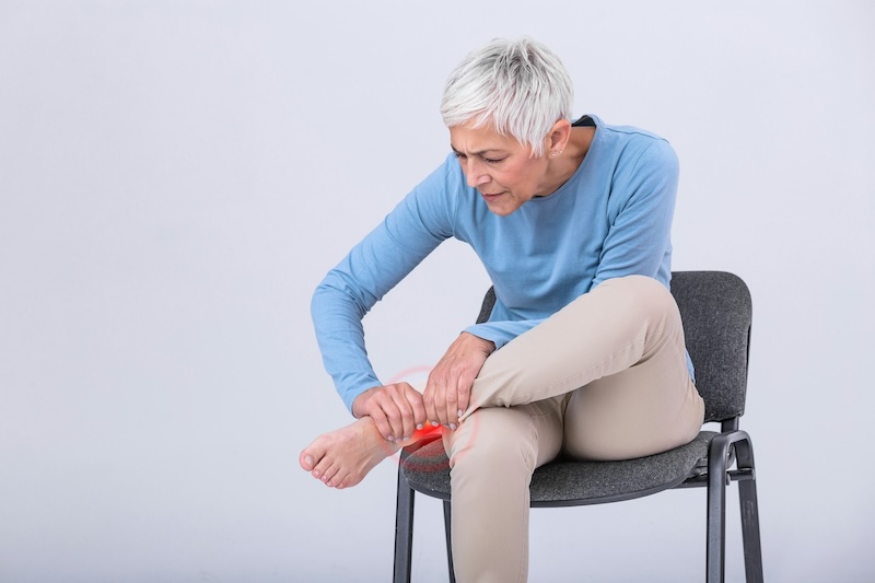 Woman with grey hair sitting in a chair, holding her ankle