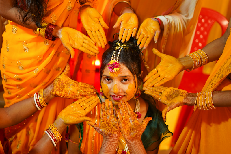 Indian woman in a wedding with hands around her covered in turmeric powder