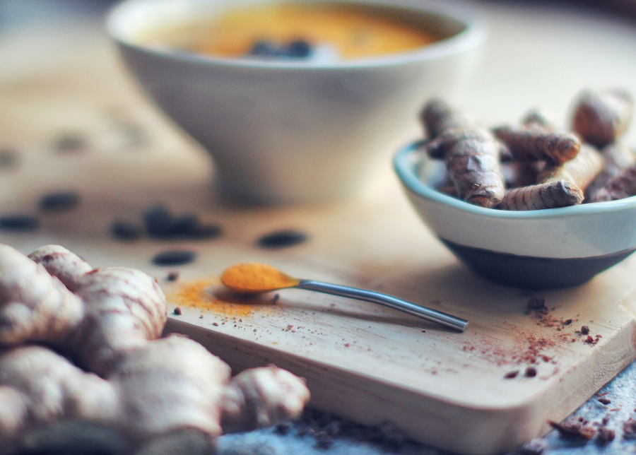 Turmeric root in a bowl, with a spoon laying in front full of turmeric powder.